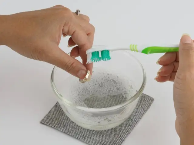 Dłoń czyści pierścionek szczoteczką do zębów w misce z pianą.