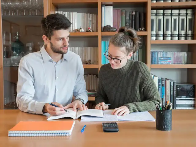 Młoda para uczy się przy biurku, otoczona książkami.