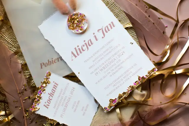 Eleganckie zaproszenia ślubne z piórami i złotymi zdobieniami.