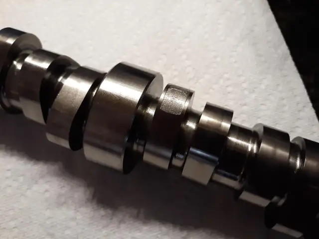 Metalowy wałek rozrządu z widocznymi śladami zużycia, wskazującymi na potencjalne objawy awarii.