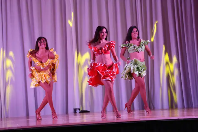 Trzy tancerki w kolorowych strojach na scenie.
