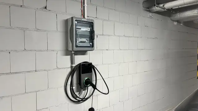 Nowoczesne gniazdo do ładowania samochodu elektrycznego Autel zamontowane na białej, ceglanej ścianie obok skrzynki z bezpiecznikami.
