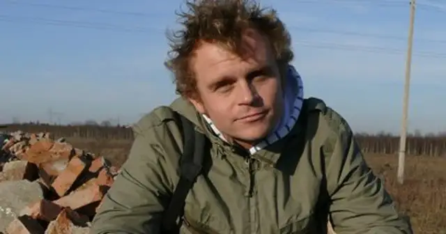 Piotr Rogucki, w otoczeniu gruzu, z charakterystyczną fryzurą, jakby inspirowany swoimi utworami.