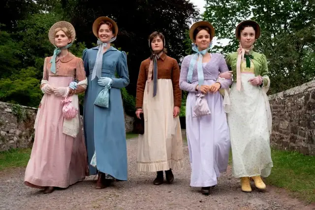 Pięć kobiet w strojach z epoki, przypominających rodzeństwo Jane Austen, spaceruje po kamienistej ścieżce.