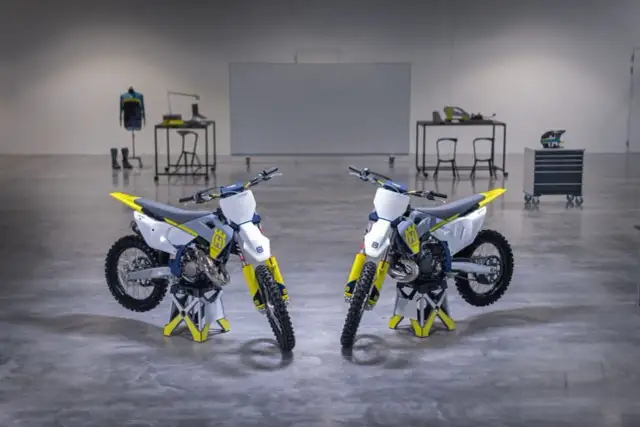 Dwa motocykle crossowe Husqvarna TC 125 w białym i żółtym kolorze stoją na stojakach.