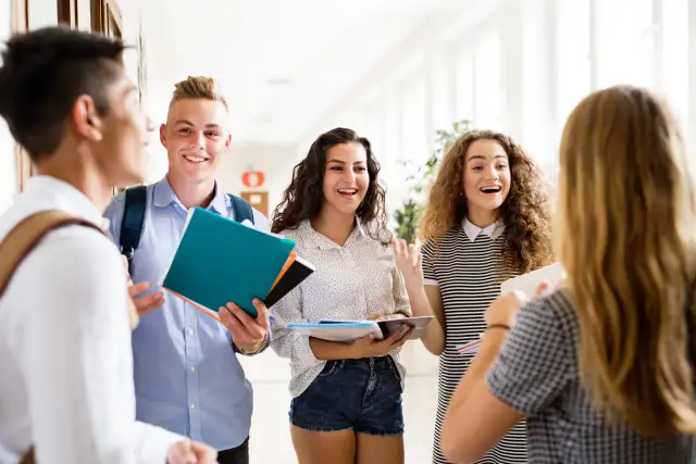 Uczniowie rozmawiają na korytarzu, trzymając książki. Czy na studium trzeba mieć maturę? To pytanie nurtuje wielu młodych ludzi.