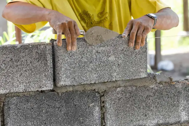 Budowniczy układa bloczki betonowe na zaprawie. Dowiedz się, jak obliczyć ile bloczków na fundament potrzebujesz.
