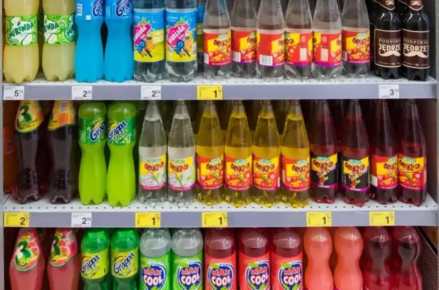Półki sklepowe z różnymi napojami gazowanymi w plastikowych butelkach.