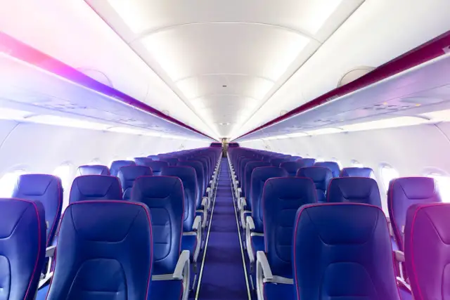 Wnętrze samolotu Wizz Air z rzędami niebieskich foteli i fioletowym oświetleniem.