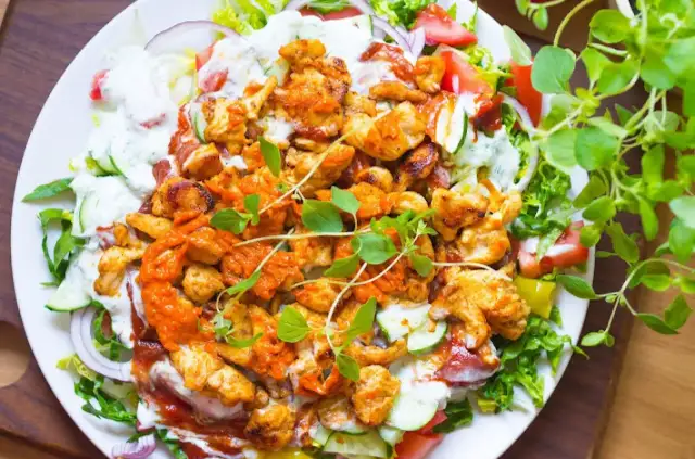 Talerz z kurczakiem kebab, warzywami, sosem i ziołami.