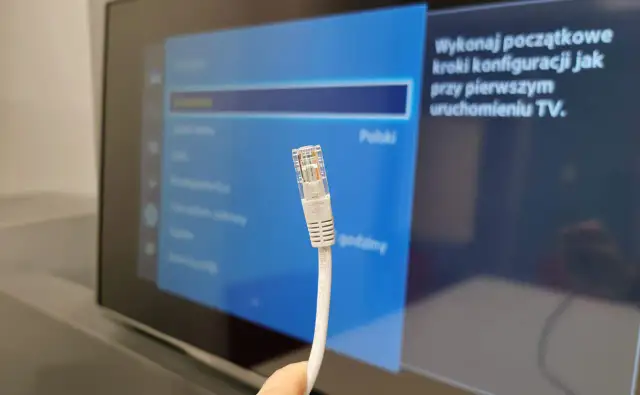 Kabel sieciowy Ethernet zbliżenie na wtyczkę RJ45 na tle ekranu telewizora z menu ustawień.