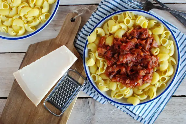 Makaron z sosem mięsnym, kawałek parmezanu i tarka na desce.