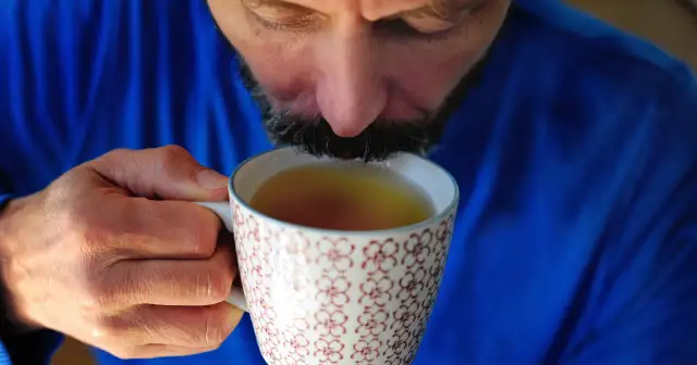 Mężczyzna w niebieskim swetrze pije herbatę z kubka. Szuka odpowiedzi, co na refluks leki, by złagodzić dolegliwości.