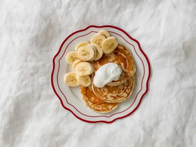 Idealne placuszki dla 10 miesięcznego dziecka: puszyste, z bananem i jogurtem naturalnym na talerzyku z czerwonym rantem.