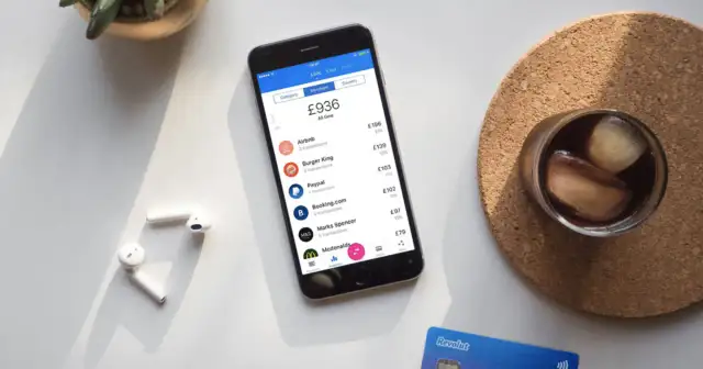 Telefon z aplikacją Revolut pokazuje transakcje, ułatwiając zrozumienie, jak płacić Revolutem za granicą. Obok leżą słuchawki i karta.