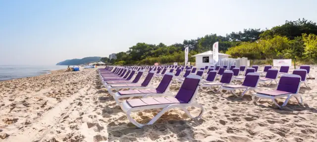 Rządki leżaków na piaszczystej plaży, idealne na tanie wczasy nad morzem dla 2 osób z wyżywieniem. W tle morze i zieleń.