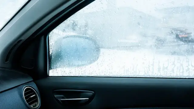 Widok z wnętrza auta na zaparowane szyby. Krople wody na szybie utrudniają widoczność drogi i lusterka bocznego.