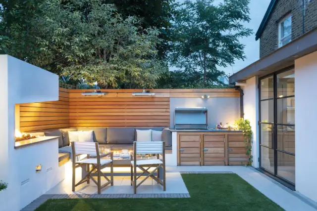 Nowoczesne aranżacje wokół tarasu: wbudowana kanapa, grill, palenisko i stylowe oświetlenie tworzą przytulną strefę relaksu.