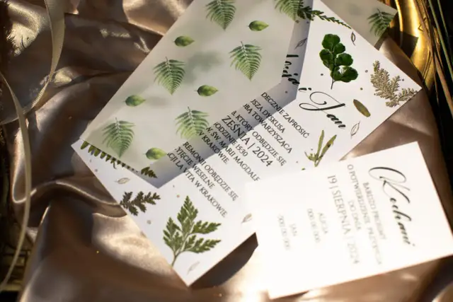 Kilka zaproszeń ślubnych z motywem paproci i liści na satynowym tle.