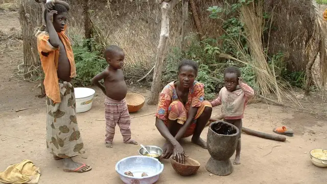 Dzieci i matka w tradycyjnej chacie w Burkina Faso. Kobieta przygotowuje posiłek, a dzieci obserwują.