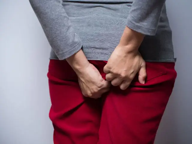 Osoba w czerwonych spodniach i szarej bluzce drapie się w okolicy odbytu. Szuka ulgi, zastanawiając się, czym smarować odbyt przy owsikach.