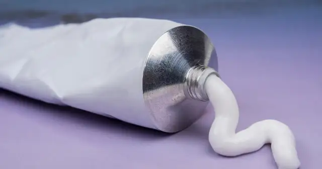 Biała pasta wydobywa się z metalowej tubki. To może być krem z witaminą F na co dzień, dla zdrowej skóry.