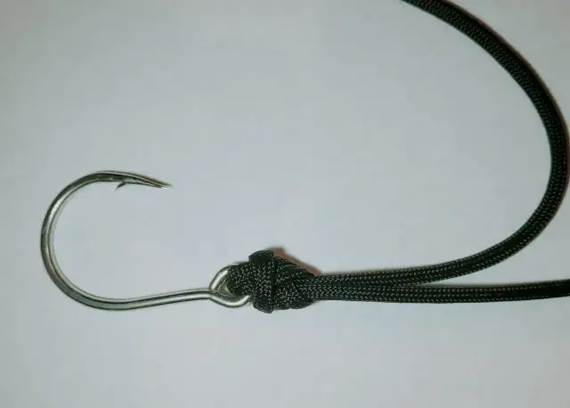 Metalowy haczyk wędkarski z zawiązanym czarnym sznurkiem na białym tle.