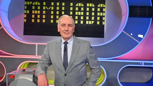 Mężczyzna w garniturze na tle planszy teleturniejowej, wyglądający na siłach i gotowy do gry, by być zdrowym jak Familiada.