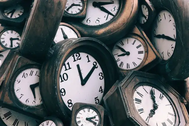 Stos starych zegarów, niektóre z rzymskimi cyframi, inne z arabskimi.