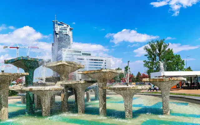 Fontanna z modernistycznymi budynkami w tle i błękitnym niebem.