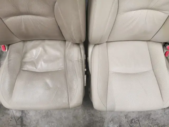 Naprawa fotela skórzanego w samochodzie. Widoczne dwa jasne, perforowane fotele, jeden z widocznymi przetarciami i zagnieceniami, drugi odnowiony.