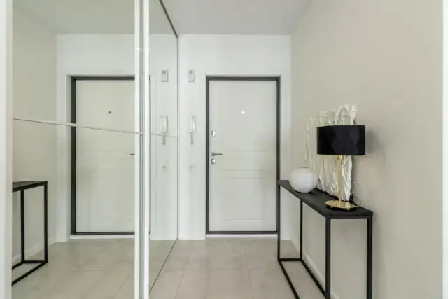 Nowoczesny wiatrołap inspiracje: białe drzwi, lustrzana szafa i elegancka konsola z lampą.