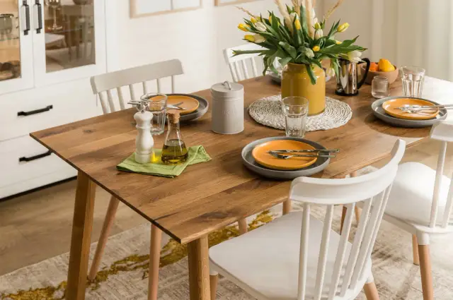 Drewniany stół z żółtymi tulipanami, naczyniami i oliwą.