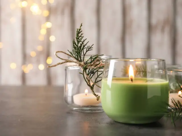 Płonące zielone i białe świece zapachowe w szklanych pojemnikach, ozdobione gałązkami.