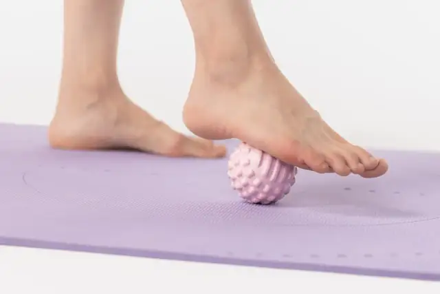 Stopa masowana różową kulką do masażu na fioletowej macie.