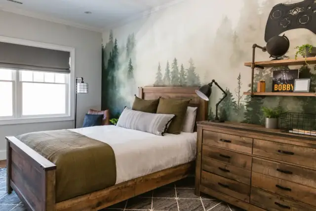 Przytulny pokój 14 latka z leśną tapetą, drewnianym łóżkiem i komodą. Na ścianie wisi gigantyczny kontroler do gier.