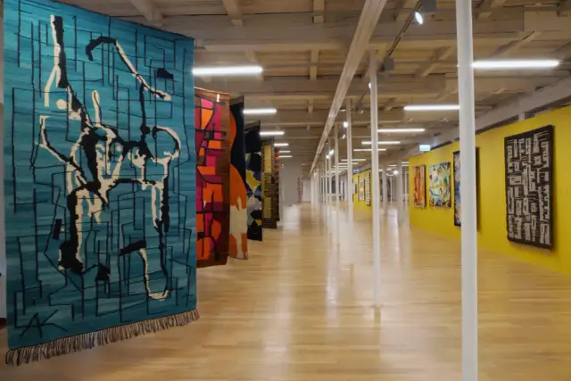 Wystawa prezentuje, kto wytwarza dekoracyjne tkaniny ścienne. Kolorowe, abstrakcyjne wzory zdobią galerię.