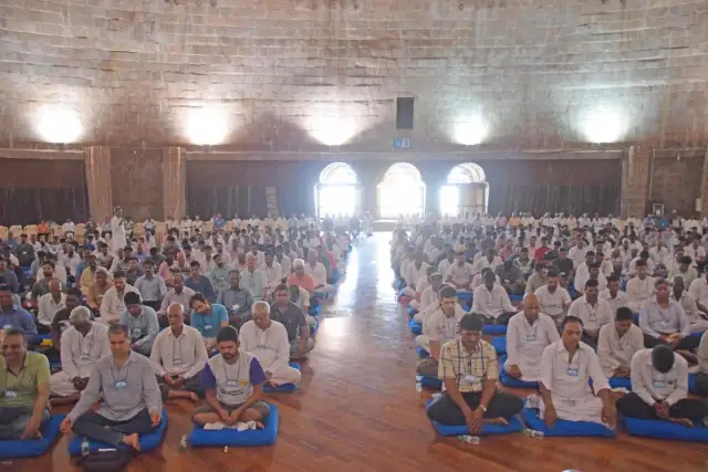 Wielka sala pełna ludzi siedzących w medytacji. To właśnie vipassana co to jest – praktyka uważności.