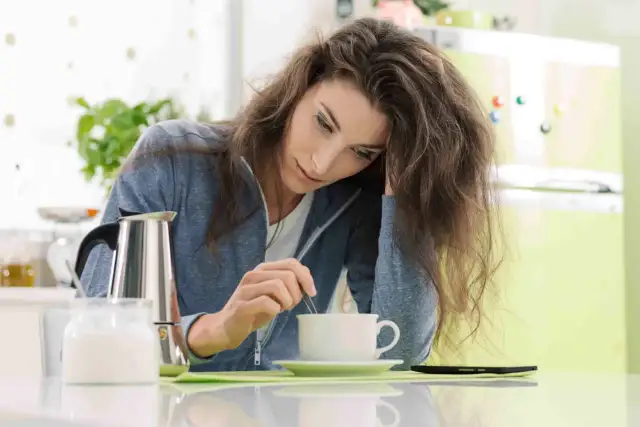 Kobieta z **stanem zapalnym organizmu** miesza kawę, czując się osłabiona.