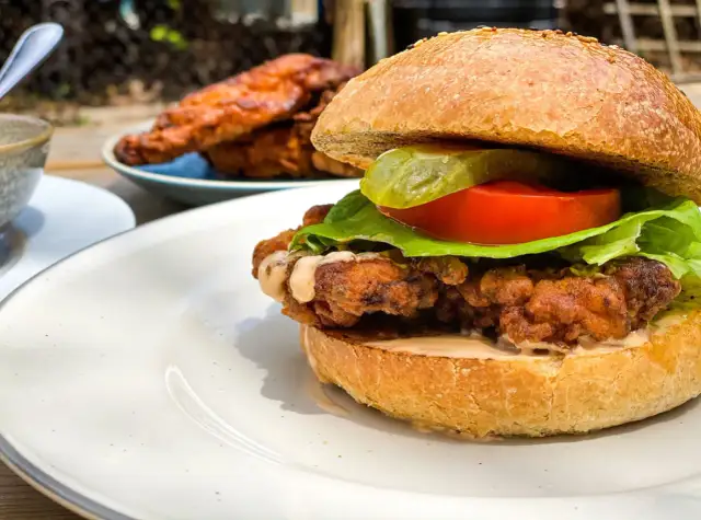 Burger maison au poulet croustillant et juteux, garni de laitue, tomate et cornichon.