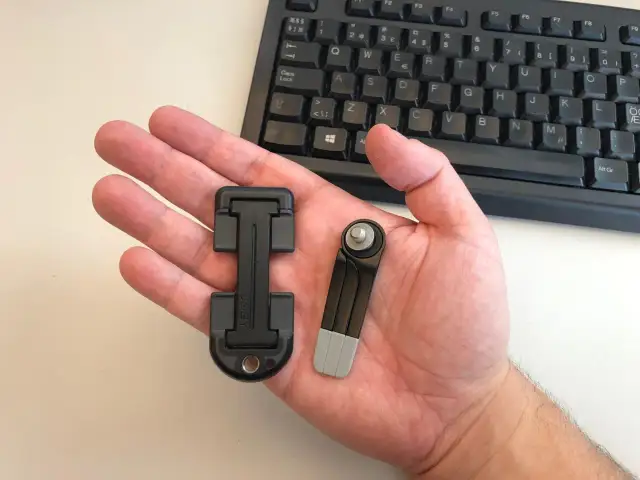 Dłoń trzymająca dwa czarne klucze Steam na tle klawiatury.