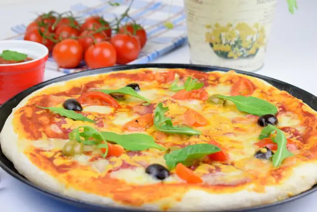 Domowa pizza z pomidorami, oliwkami i rukolą na czarnym talerzu.