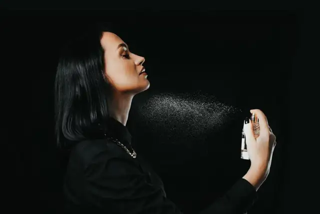 Kobieta rozpyla perfumy na szyję na czarnym tle.