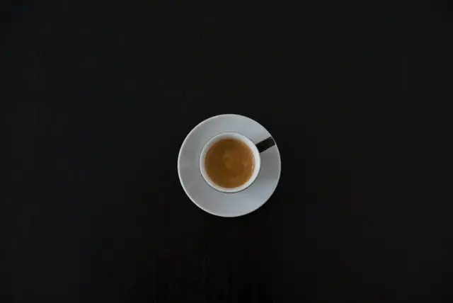 Czarna filiżanka espresso na białym spodeczku na ciemnym tle. Może symbolizować początek walki z objawami odstawienia kofeiny.