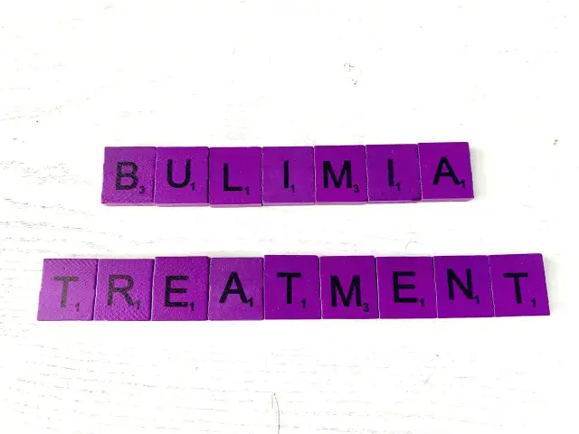 Fioletowe kafelki z literami układają słowa "BULIMIA TREATMENT". Bulimia co to? Leczenie jest kluczowe.