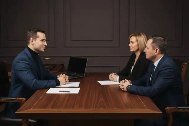 Trzy osoby przy drewnianym stole, laptop, dokumenty. Prawnik przedstawia potwierdzenie za zgodność z oryginałem.