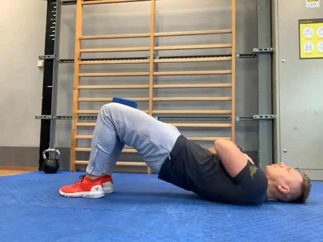 Mężczyzna wykonuje ćwiczenie z podniesioną miednicą, co może być pomocne przy dyskopatii. Unikaj gwałtownych ruchów.