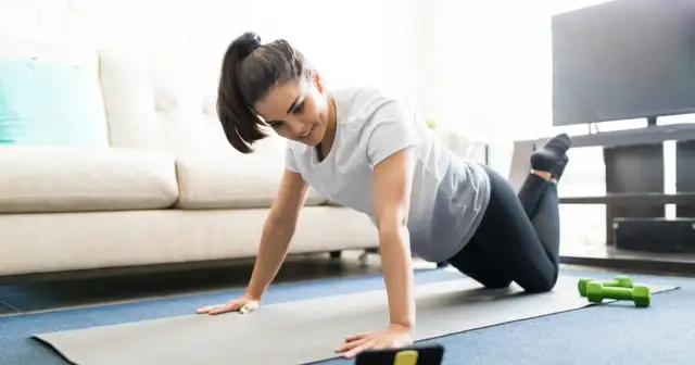 Kobieta na macie do ćwiczeń wykonuje pompki, patrząc na telefon. Czy można ćwiczyć z kaszlem? Zależy od samopoczucia.