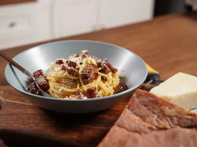 Miseczka spaghetti carbonara z boczkiem i parmezanem, obok kawałki sera i boczku.