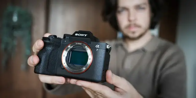 Mężczyzna trzyma aparat Sony Alpha z widocznym obiektywem i mocowaniem E-mount.